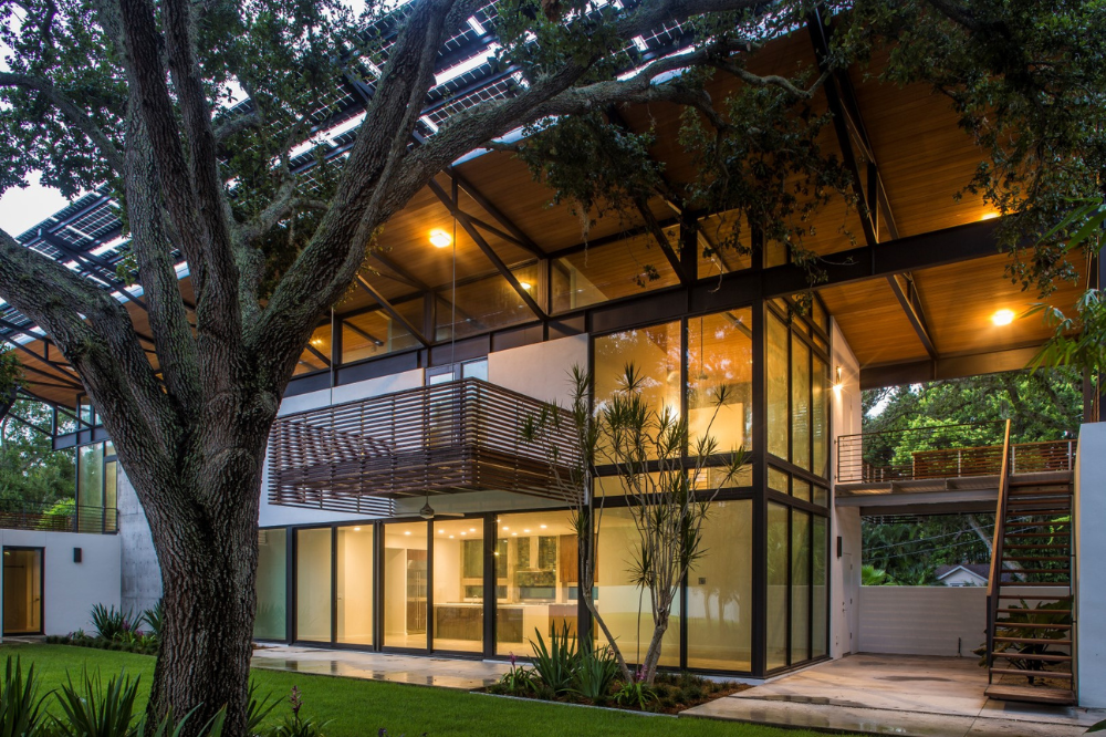 Fachada moderna de una casa con grandes ventanales iluminados y jardín